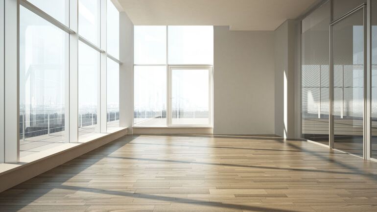 Lyst og tomt rom med store vindusflater og tregulv som slipper inn rikelig med dagslys.