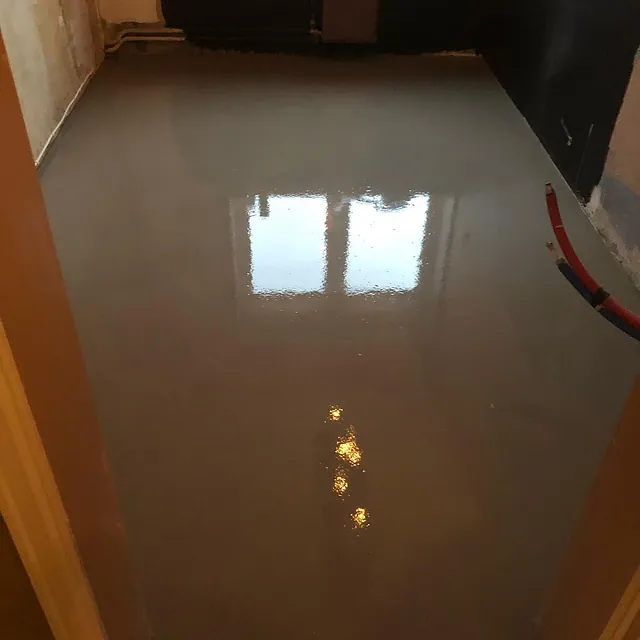 Rom med nylagt, speilblankt selvutjevnende gulv som reflekterer vindu og lys fra tak.