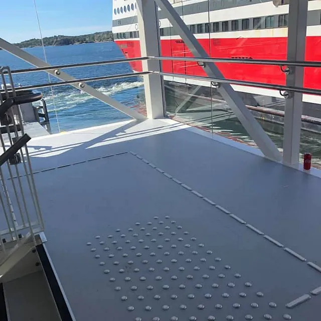 Inngangsområde med lysegrått gulv og taktile punkter, store vinduer med utsikt mot hav og ferge.