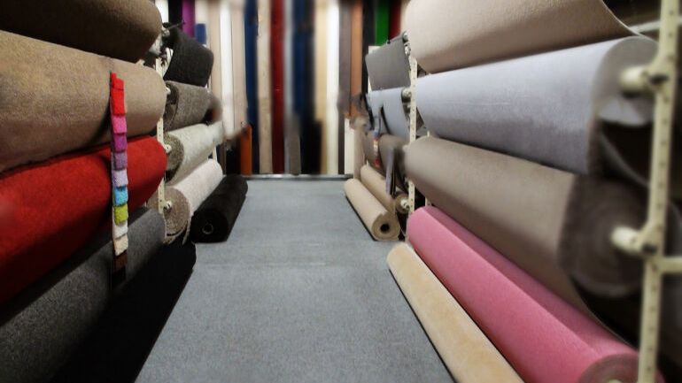 Ruller med heldekkende tepper i ulike farger og teksturer på utstilling i teppebutikk.